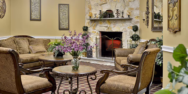 Cozy sitting area with upholstered chairs and sofas arranged around a stone fireplace and coffee tables with floral arrangements.