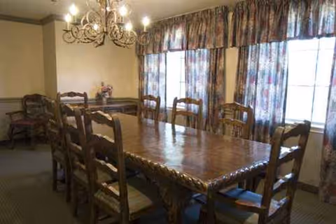 A long wooden dining table with high back chairs in a bright communal dining room.