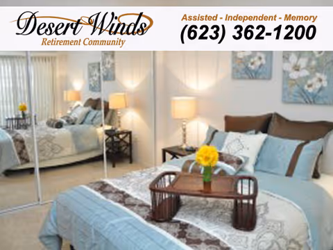 A neatly made bed in a bedroom with light blue and brown bedding, a wooden tray with a yellow flower vase on the bed, two bedside tables with lamps, and mirrored closet doors reflecting the room.