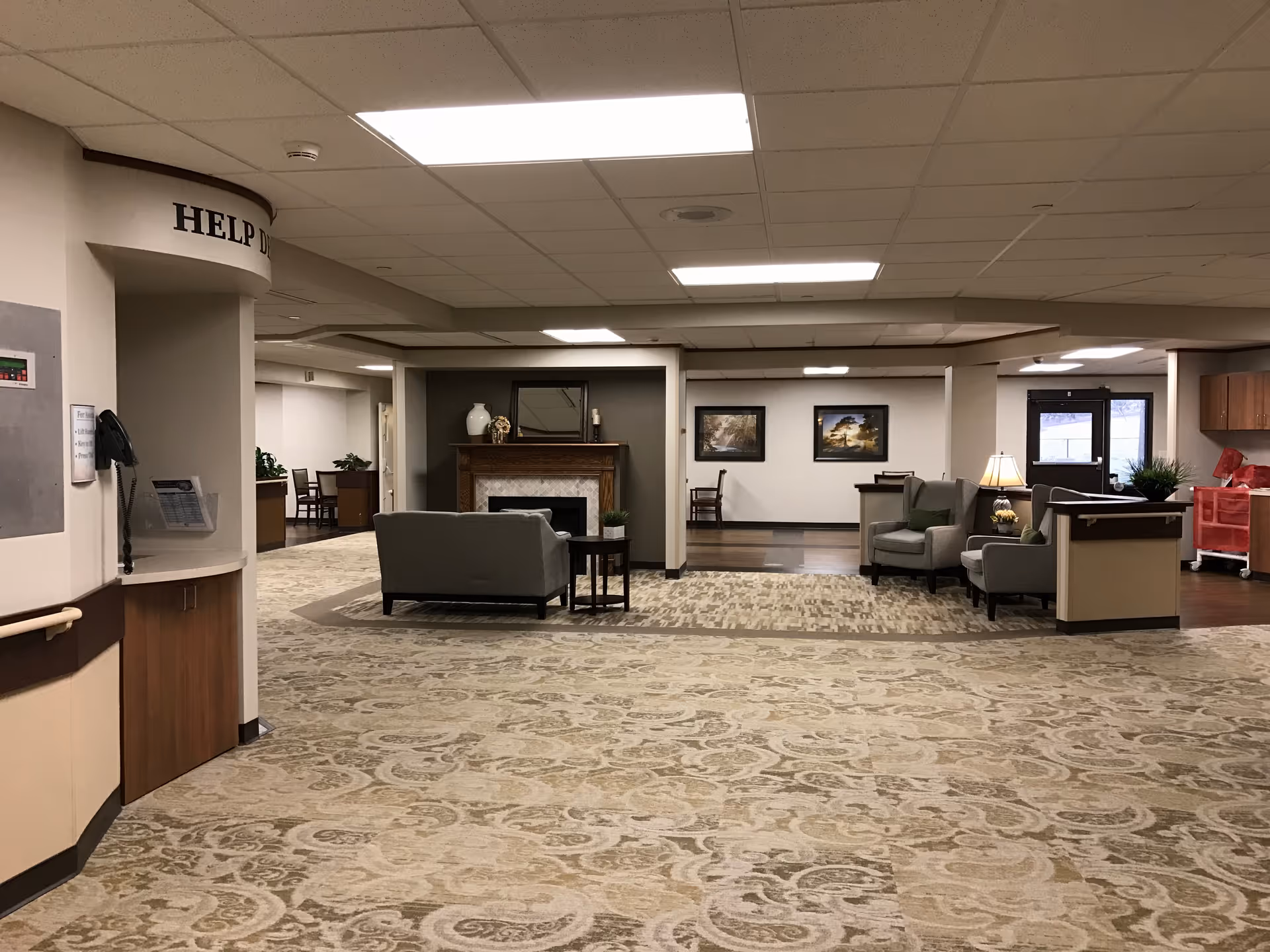 Spacious senior living common area with sofas, armchairs, a fireplace, lamps, and patterned carpet.