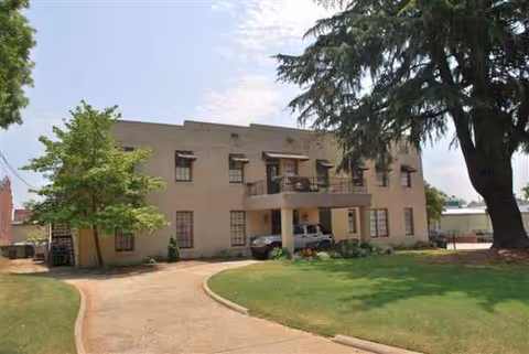 Two-story beige senior living building with curved driveway, lawn, and trees in front.