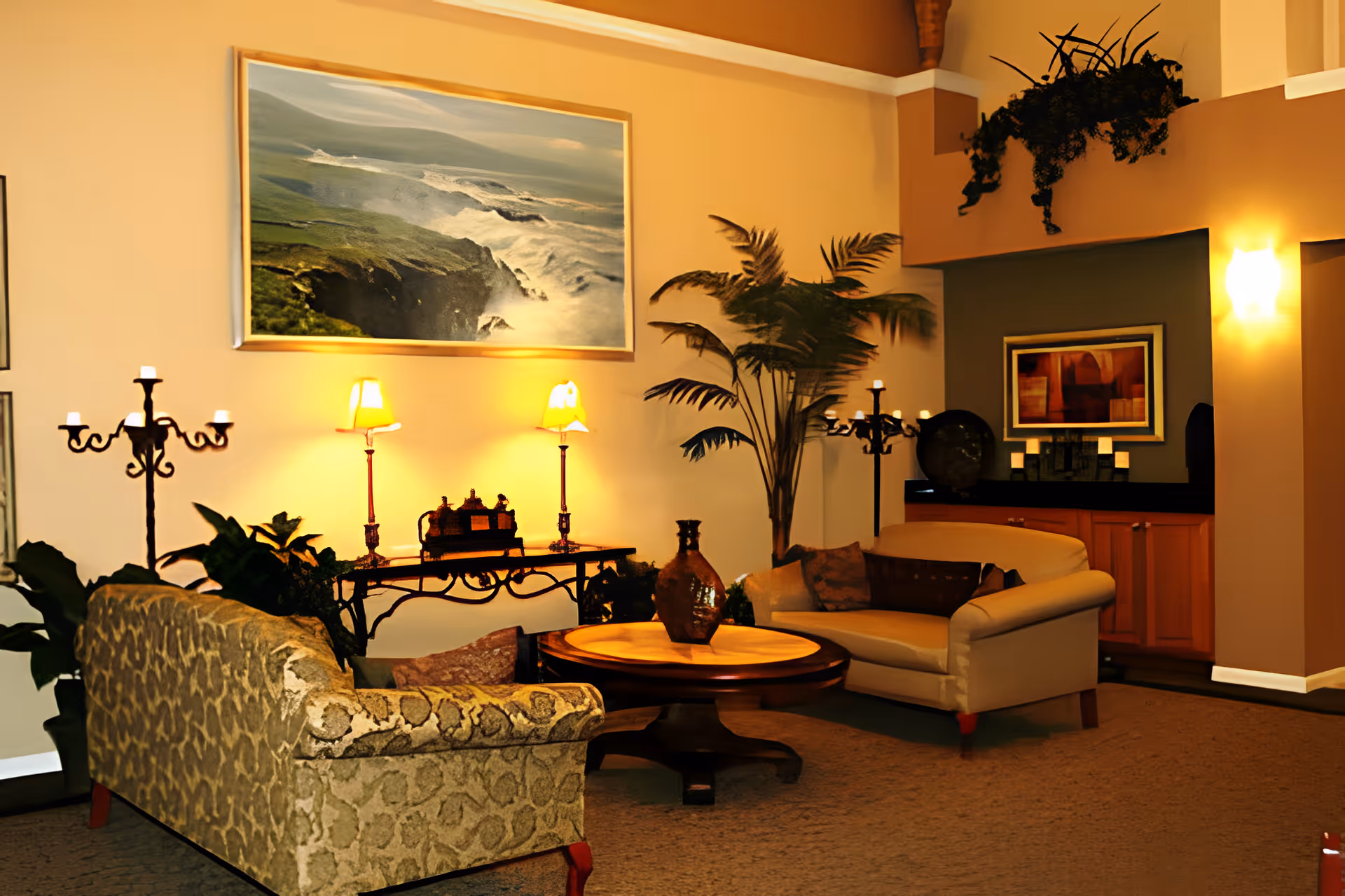 Cozy senior living room lounge with sofas, a round coffee table, lamps, potted plants and framed artwork on the walls.