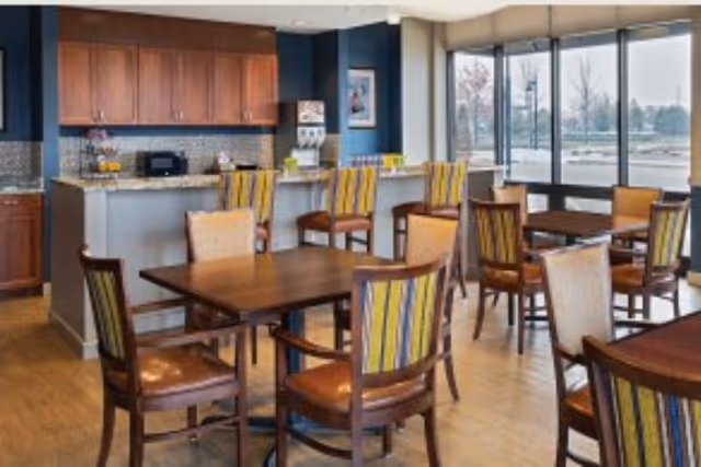 Dining area with wooden tables and striped-upholstery chairs, a countertop service area, and large windows.