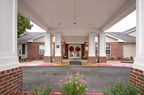 Covered porte-cochère entrance with white columns and brick facade leading to double glass doors adorned with wreaths.