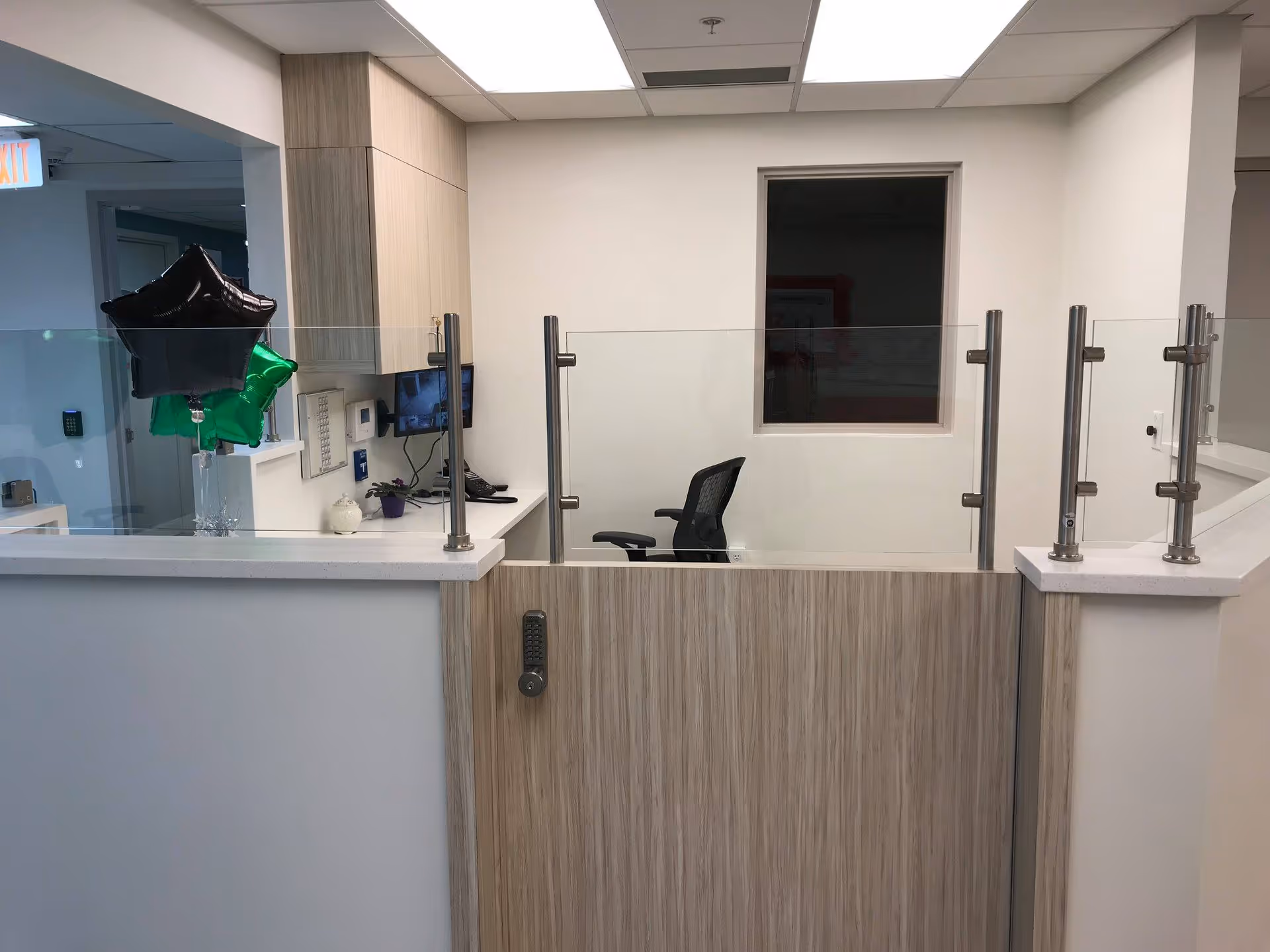 Interior reception desk area with a glass divider, office chair, countertop and balloons.