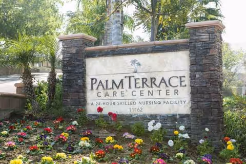 Front exterior sign for Palm Terrace Care Center surrounded by stone pillars and flowering plants.