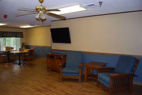 Common living area with blue upholstered chairs, wood tables, and a wall-mounted TV.