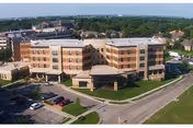 Aerial view of a multi-story senior living facility named Lakeview Village, surrounded by parking lots, roads, and greenery under a clear sky.