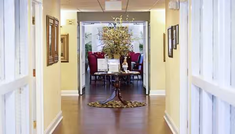 A hallway leads to seating area with a tall plant centerpiece in a senior living facility.