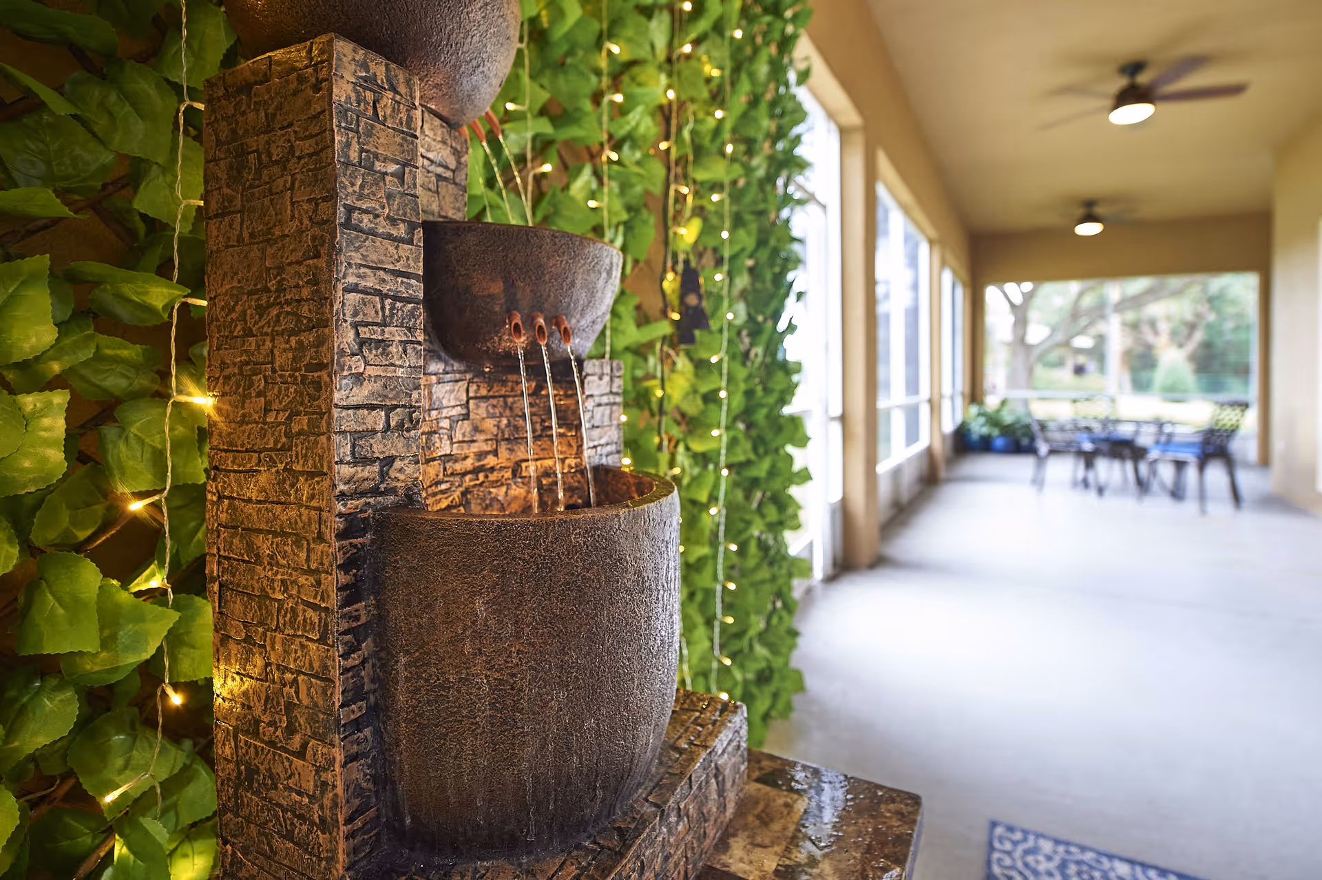 Decorative tiered water fountain beside a vertical green wall on a covered patio with seating visible in the background.