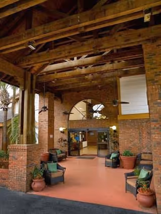Covered brick entrance with exposed wooden beams, seating, potted plants, ceiling fans, and double glass doors.
