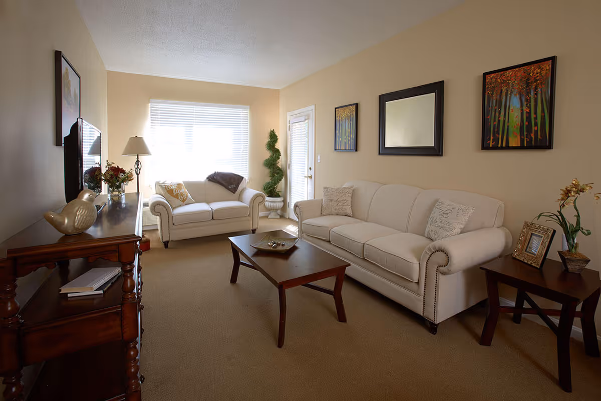 Bright living room with two beige sofas, a wooden coffee table, TV console and wall art.