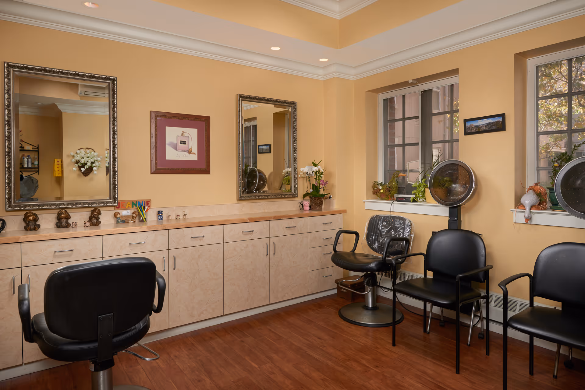 Small hair salon in a senior living facility with styling chairs, hooded dryers, mirrors, and cabinetry.