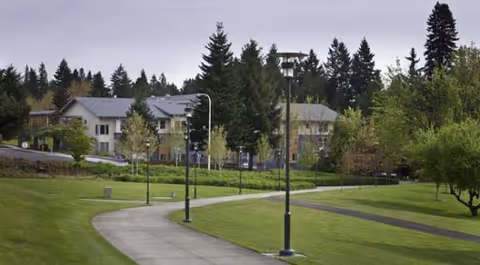 Curved walkway winds through green lawns with lampposts toward Creekside Woods senior living buildings.