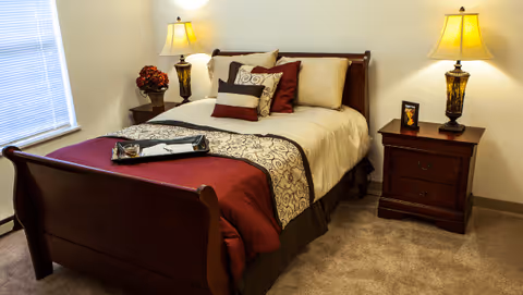 Neat bedroom with a wooden sleigh bed made up with cream and burgundy bedding, two bedside tables and lamps.