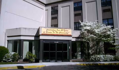 Front exterior of Brookhaven Health Care Facility with glass doors, sign, and landscaped bushes.