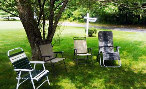 Outdoor lawn with four folding chairs around a tree near a white sign