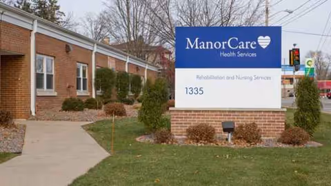 Brick exterior of a senior care facility with a blue ManorCare sign and landscaping.