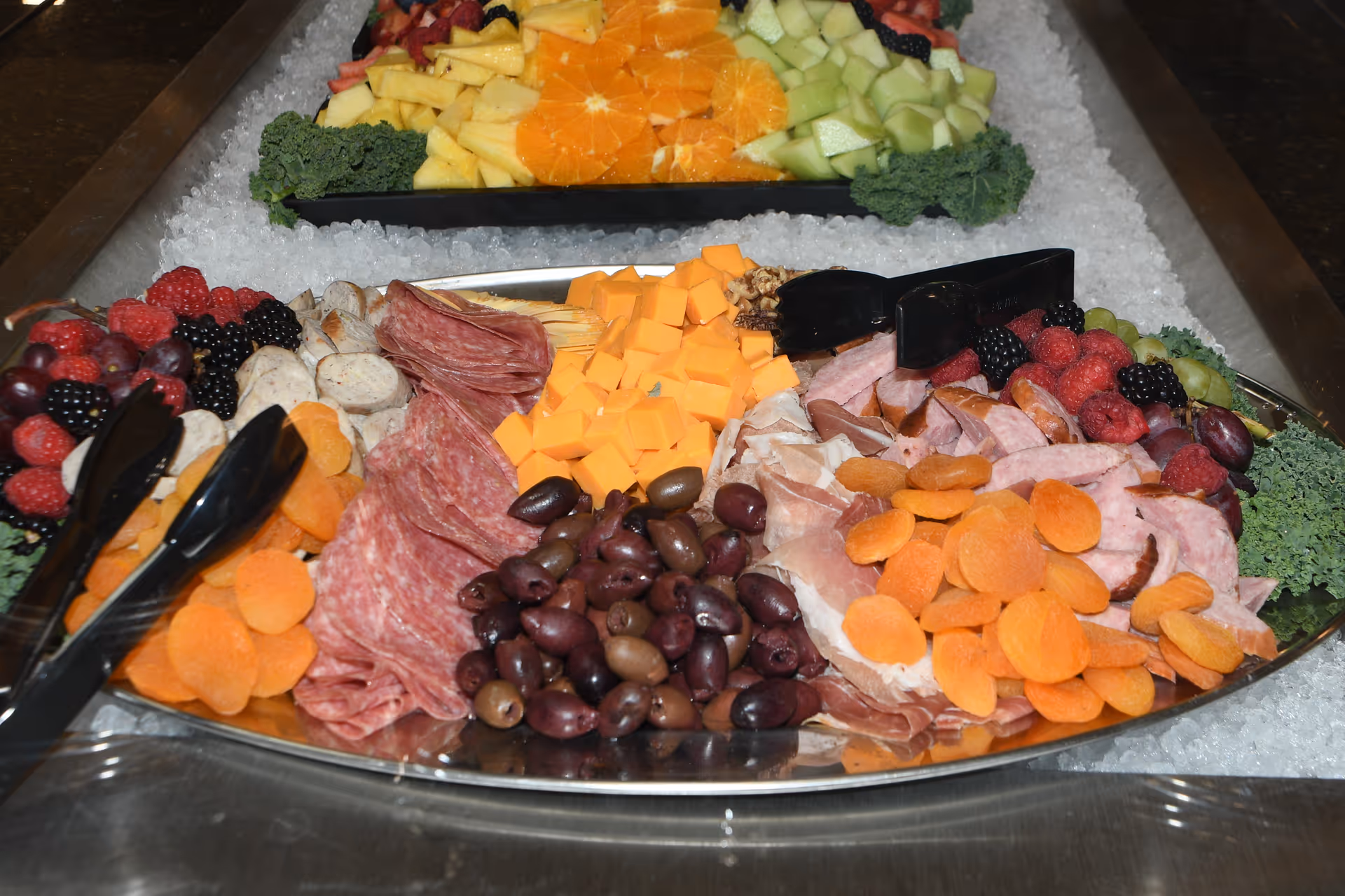 A chilled charcuterie platter with cubes of cheddar, olives, cured meats, dried apricots and berries arranged on ice.