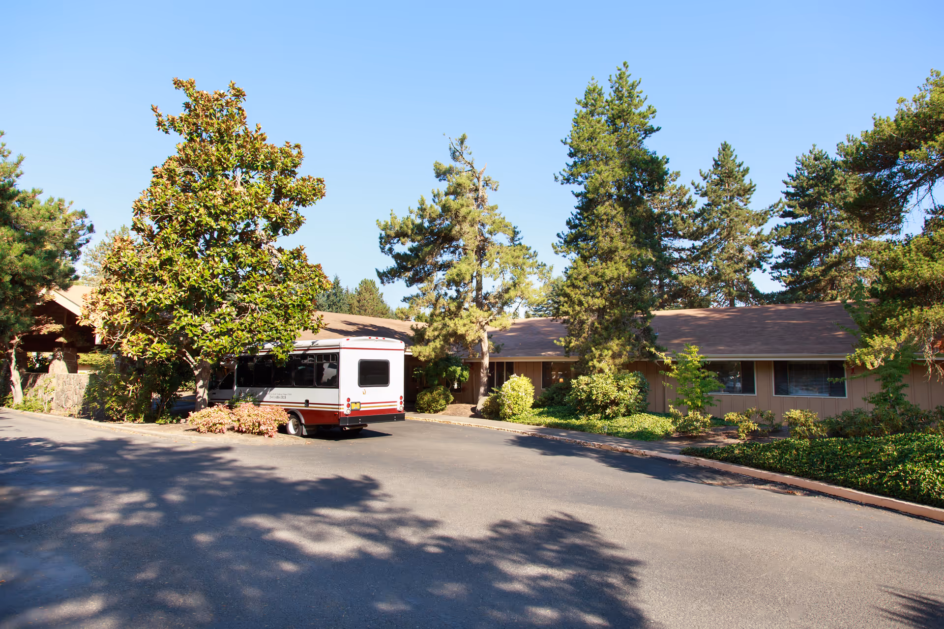 Single-story healthcare facility front with trees and a white-and-red shuttle bus parked in the driveway.