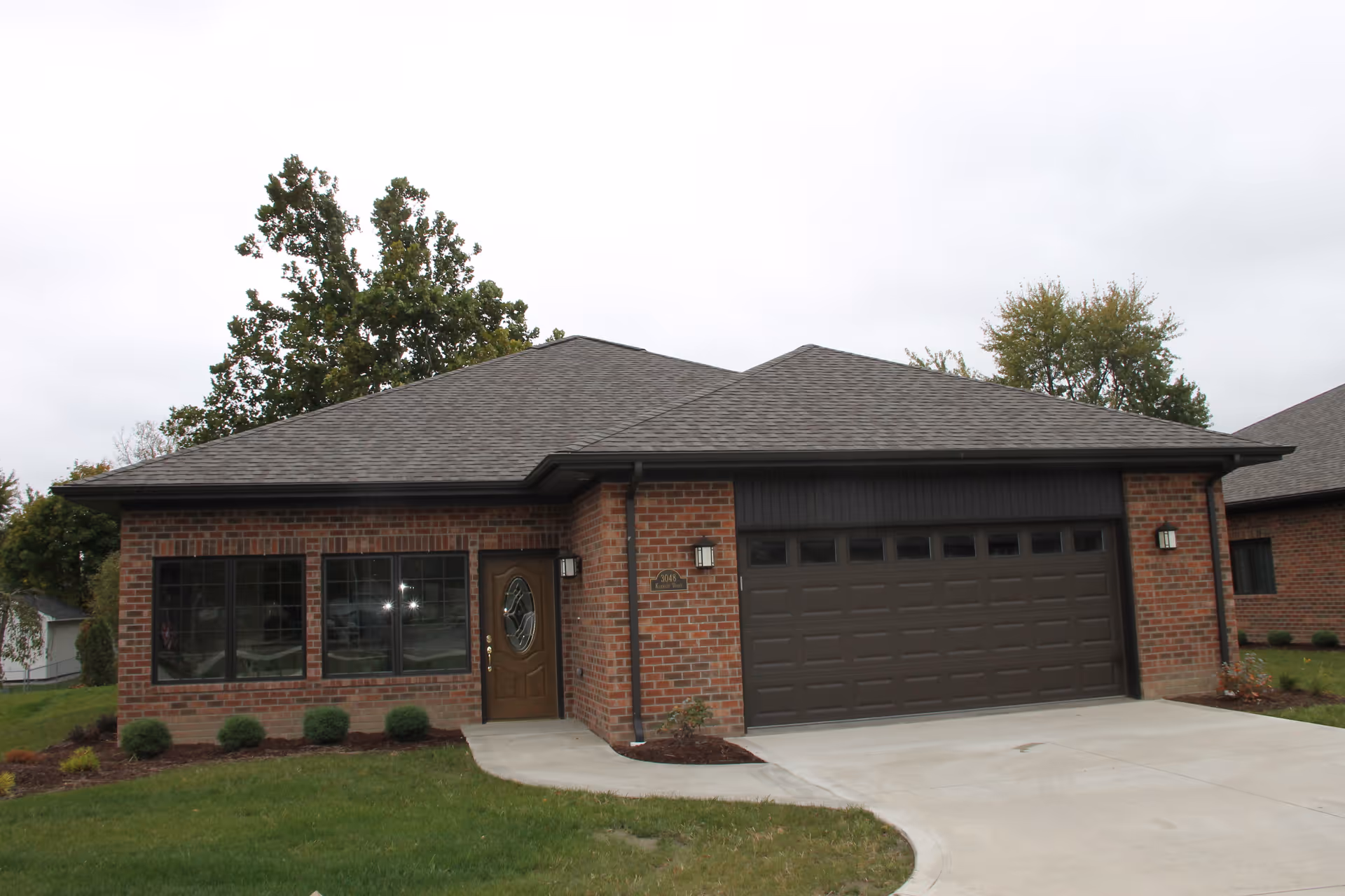 Single-story brick house with an attached two-car garage, front door, windows, and a small lawn.