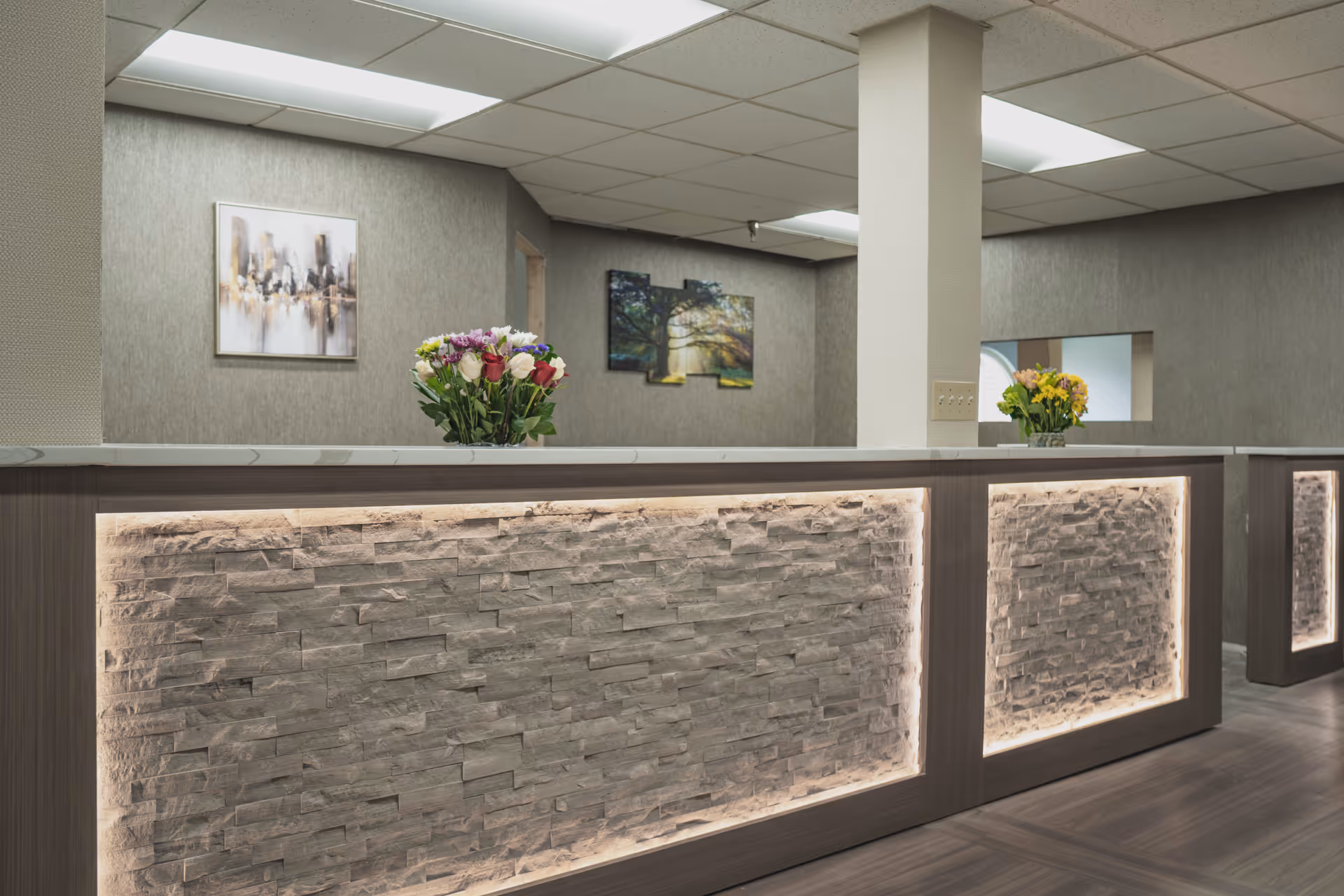 Modern reception desk with illuminated stone panels, fresh flower arrangements, and framed artwork on the walls.