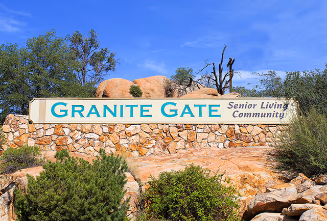 Stone sign for Granite Gate Senior Living Community set against a backdrop of rocks, trees, and a clear blue sky.