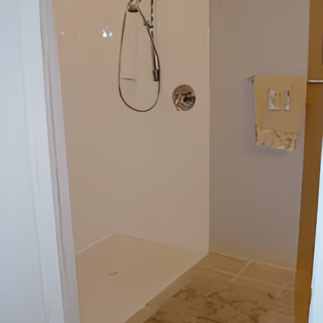 Empty walk-in shower with a handheld showerhead and a towel hanging on the wall.