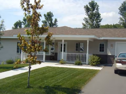 Single-story senior living facility with a front porch, manicured lawn, and driveway.