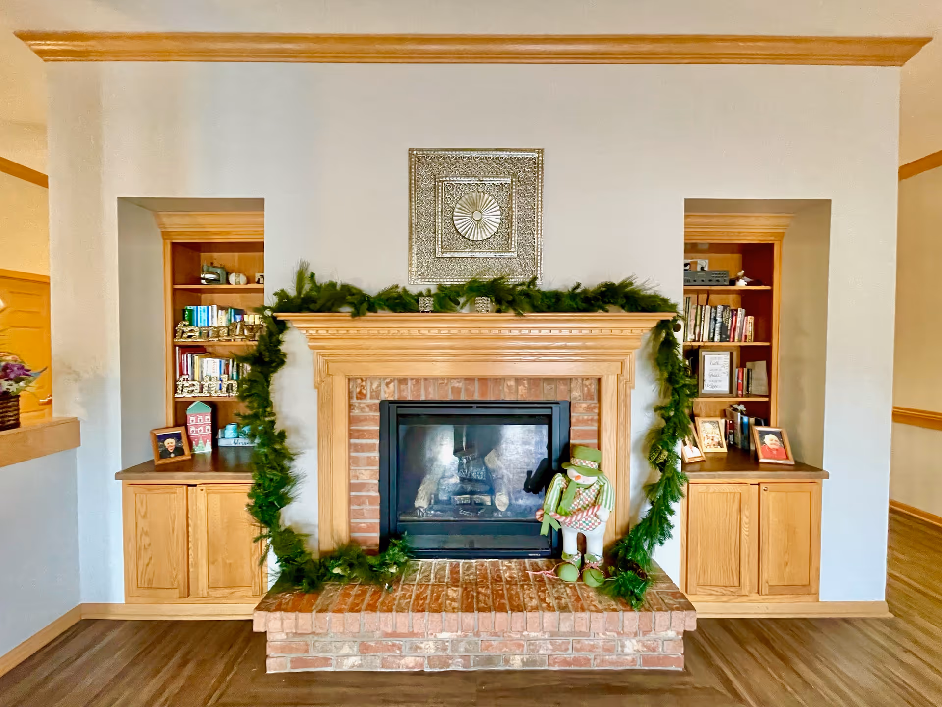Fireplace with brick hearth and garland, flanked by wooden bookcase cabinets in a cozy living room.