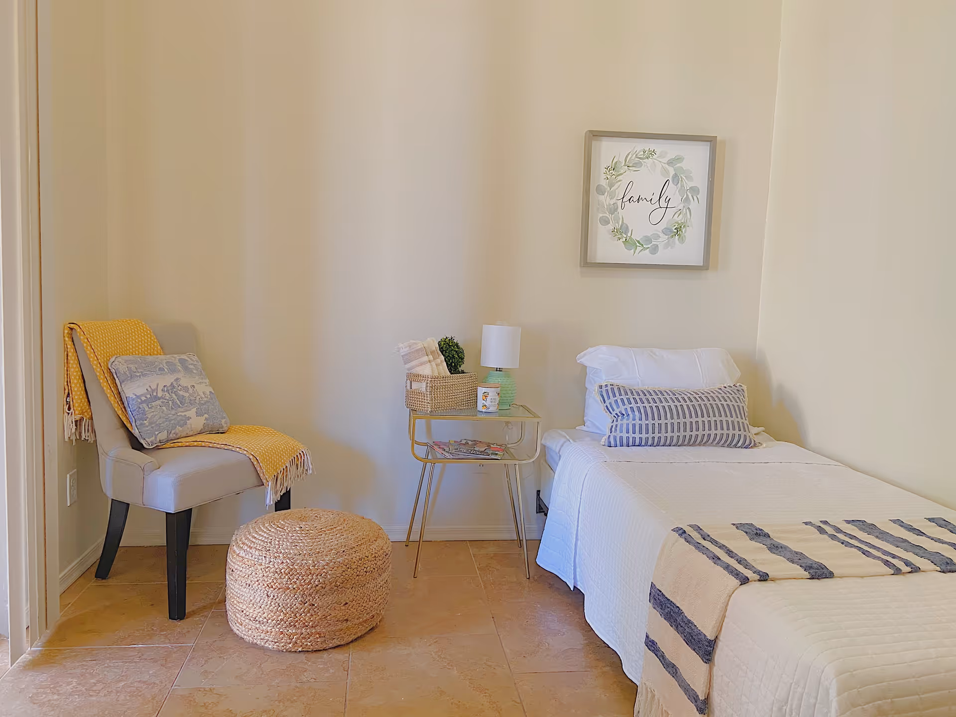 Cozy single-occupancy bedroom with a bed, bedside table and lamp, an accent chair with a yellow throw, and wall art.