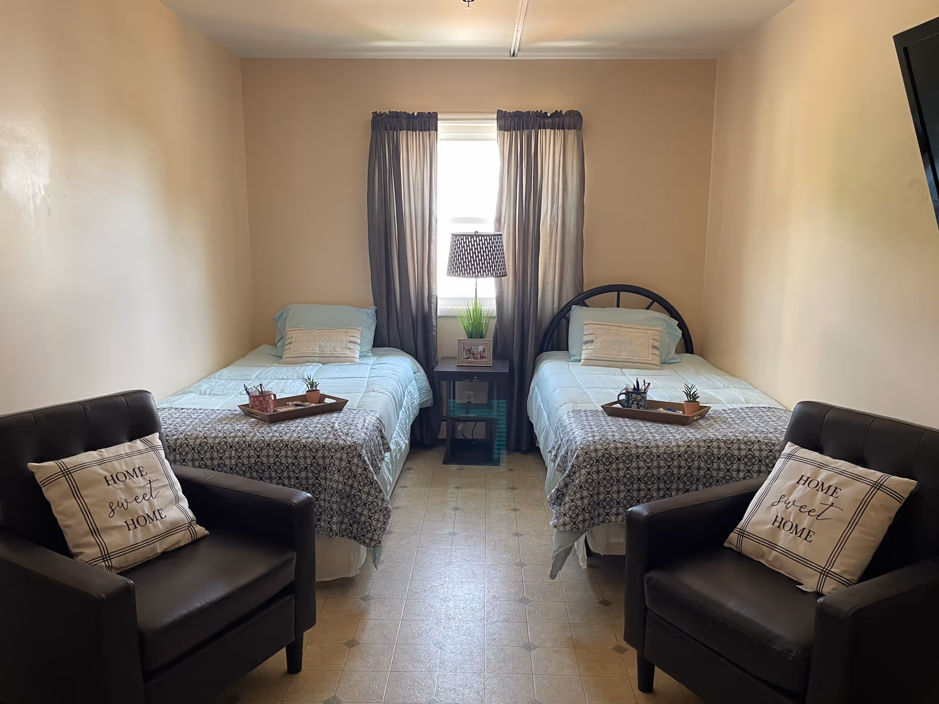 Two twin beds with matching bedding flank a window, with a central nightstand and two chairs.