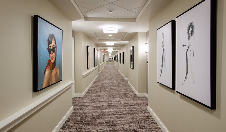 A long carpeted interior hallway with framed artwork on both walls and ceiling lights.