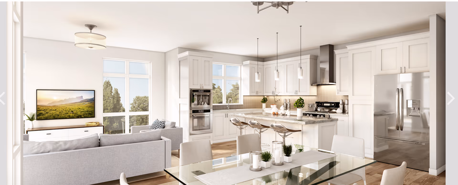 Bright and modern open-concept living space featuring a kitchen with white cabinetry, stainless steel appliances, and a large island with bar stools. Adjacent to the kitchen is a dining area with a glass table and chairs, and a living room with a gray sofa and a wall-mounted TV. Large windows allow natural light to fill the room.