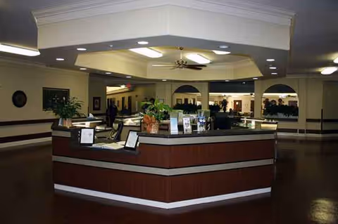 Interior of a senior living lobby with a curved reception desk and potted plants.