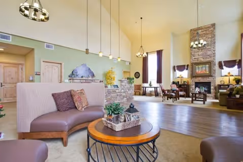 Spacious senior living common lounge with high ceilings, seating areas, a coffee table, and a stone fireplace.