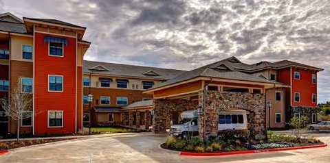Exterior view of a multi-story senior living facility building with a covered entrance and stone pillars under a cloudy sky.