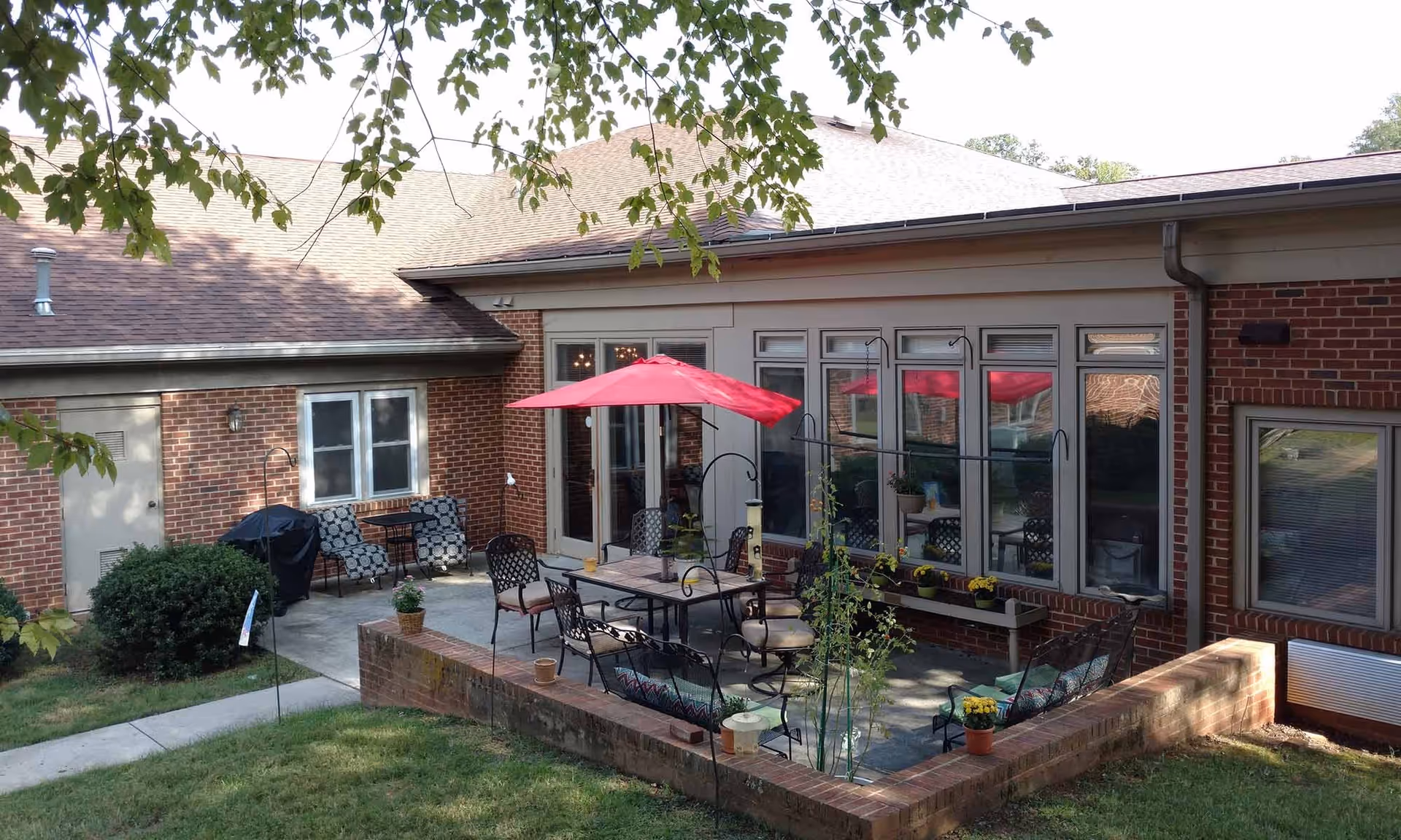 Brick building courtyard patio with a dining table, chairs, a red umbrella, potted plants, and surrounding windows.