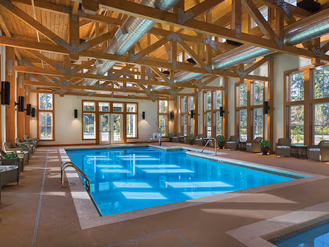 Indoor swimming pool in a timber‑beamed room with large windows and seating along the sides.