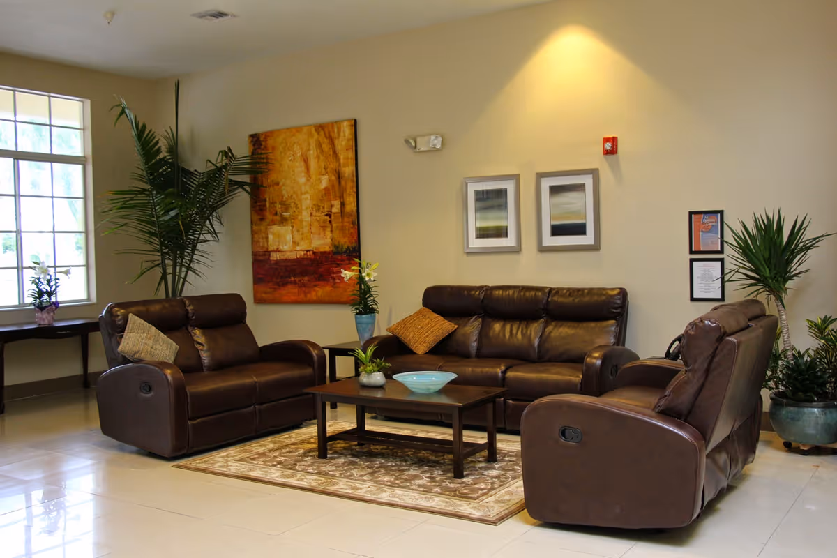 A lounge with three brown leather recliners arranged around a coffee table, decorative plants, and framed wall art.