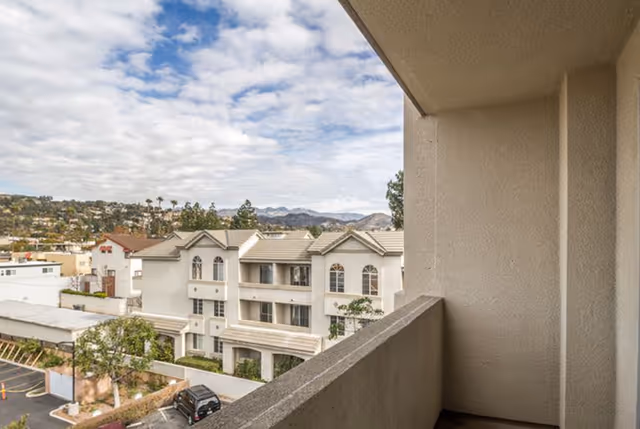 Balcony view overlooking neighboring multi-story residential buildings with hills in the distance.