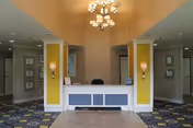 Reception desk and lobby area with a chandelier, yellow-accented columns, and patterned carpet.