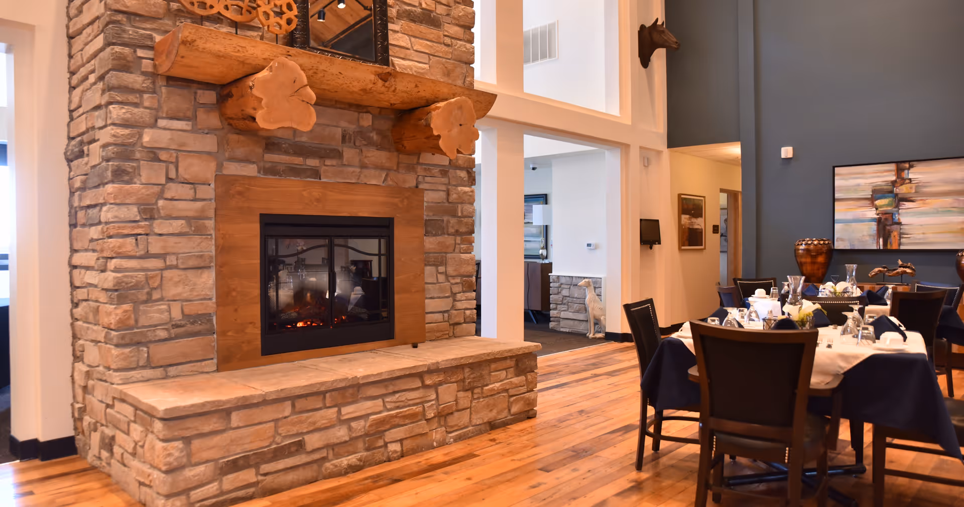 Dining room interior with a stone fireplace, wooden floors, and tables set for a meal.
