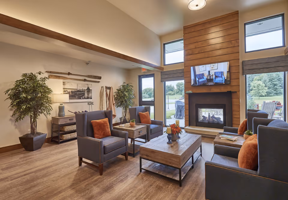 Bright, modern common living room with armchairs, a coffee table, fireplace and large windows overlooking greenery.