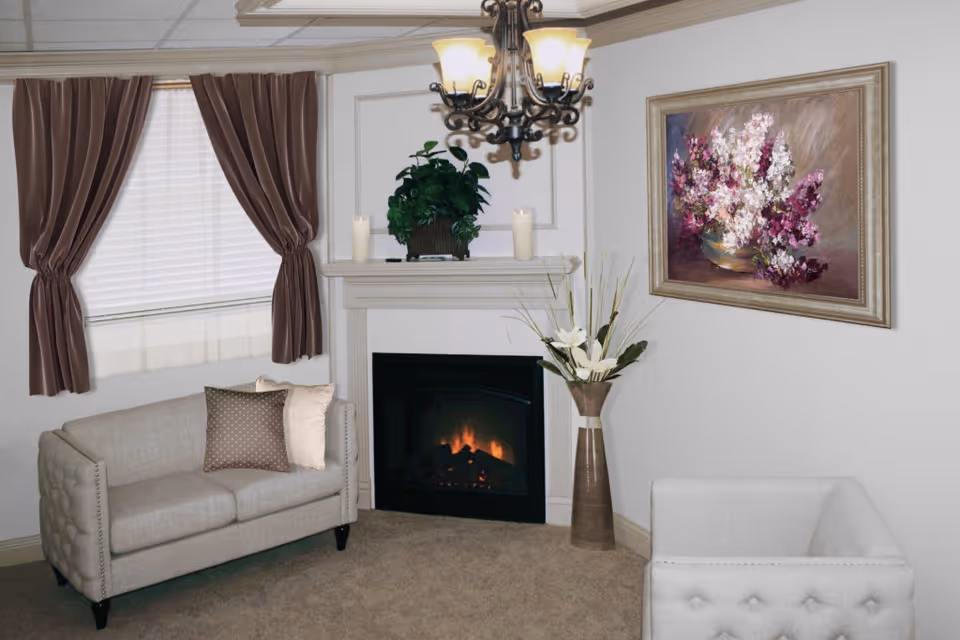 Cozy living room with a lit fireplace, two upholstered sofas, a chandelier, floral artwork, and a curtained window.