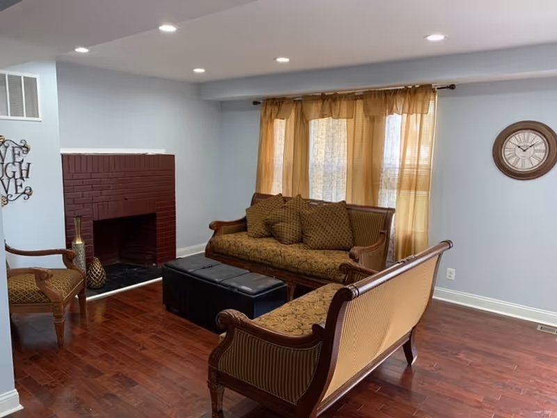 Cozy living room in a senior facility with sofa, chairs, fireplace, and curtains.
