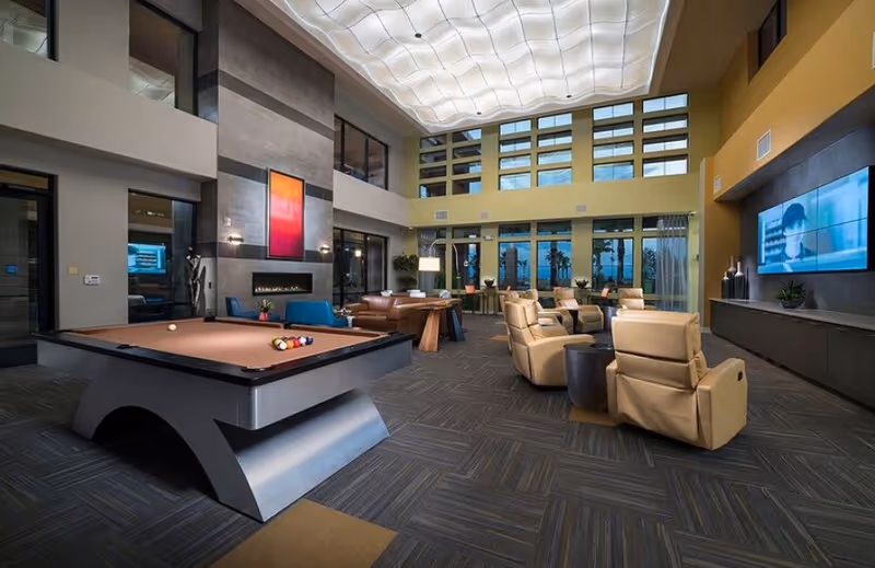 Spacious communal lounge with a pool table, reclining chairs, sofas, large TV, and tall windows under a sculpted ceiling.