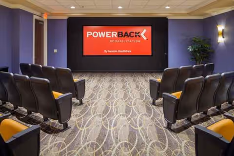 A conference room with rows of black chairs facing a PowerBack Rehabilitation screen.