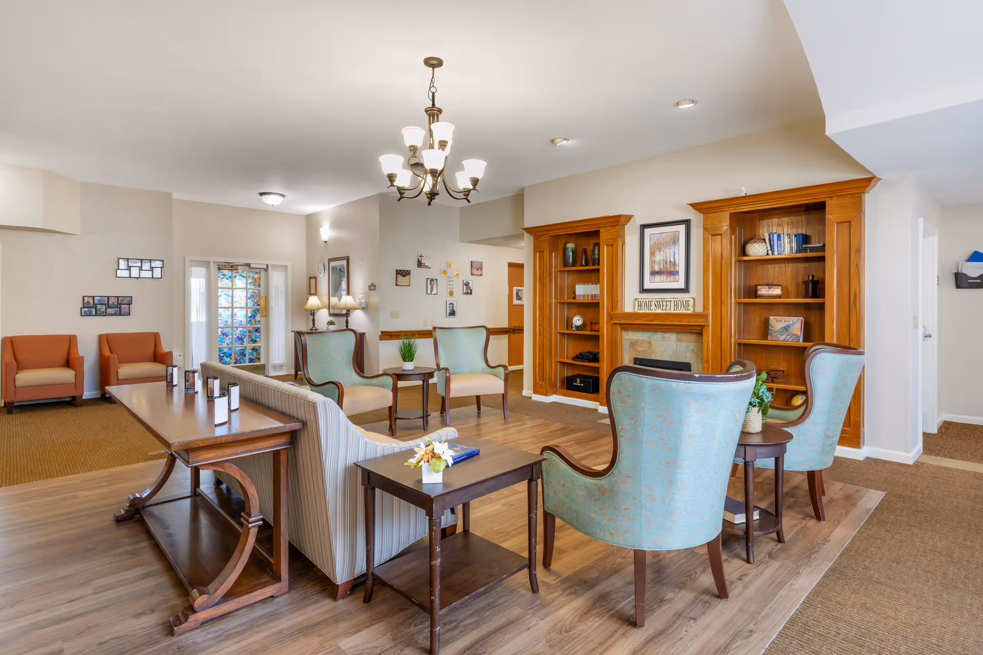 Bright, furnished communal living room with armchairs, sofas, bookshelves and a fireplace.