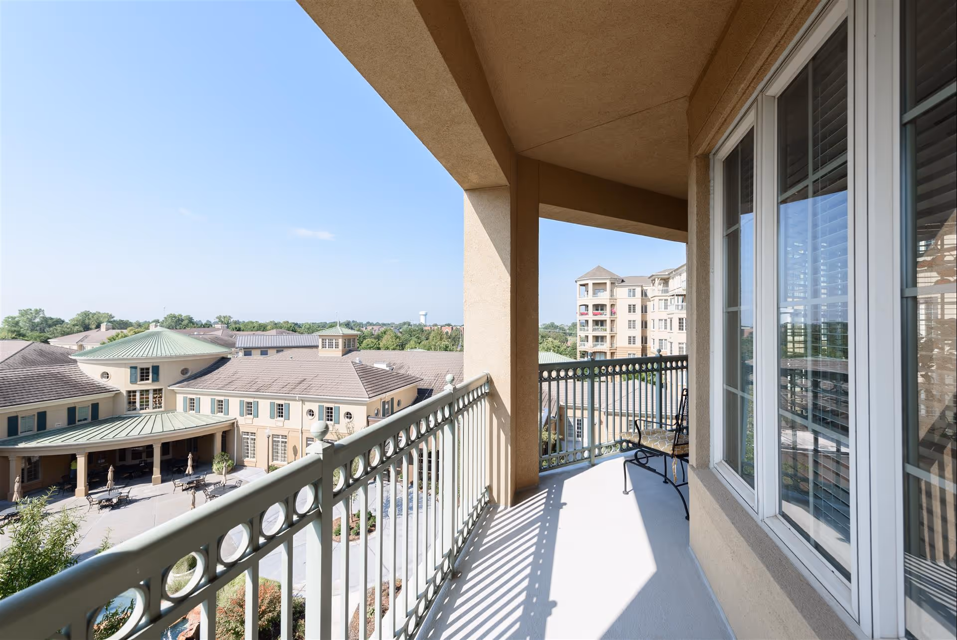 Covered balcony with a metal railing and chair overlooking the facility courtyard and neighboring buildings.